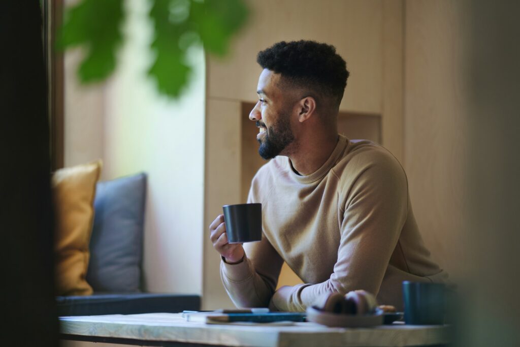 Happy young man with coffee sitting indoors in a tree house, weekend away and individual traveling
